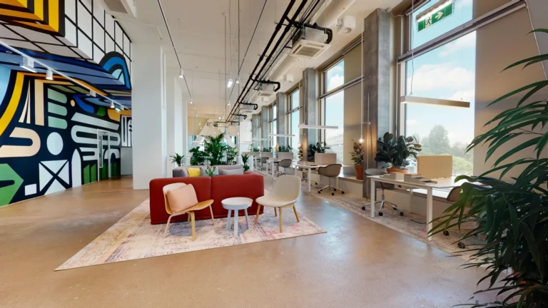Coworking-Fläche im DC Tower 3 in der Donau City Wien: Lounge mit rotem Sofa und Arbeitsplätze an der Fensterfront