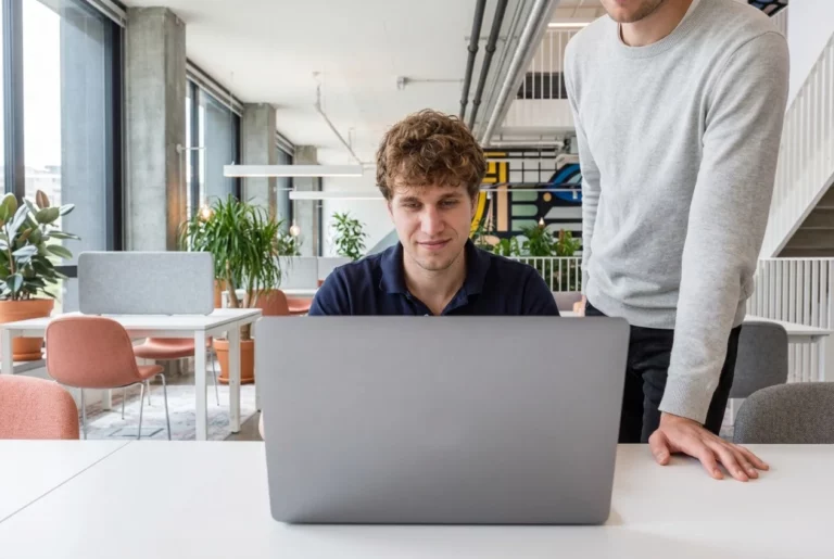 Elias Stehrer sitzt am Laptop, ein Kollege steht daneben und schaut mit auf den Bildschirm